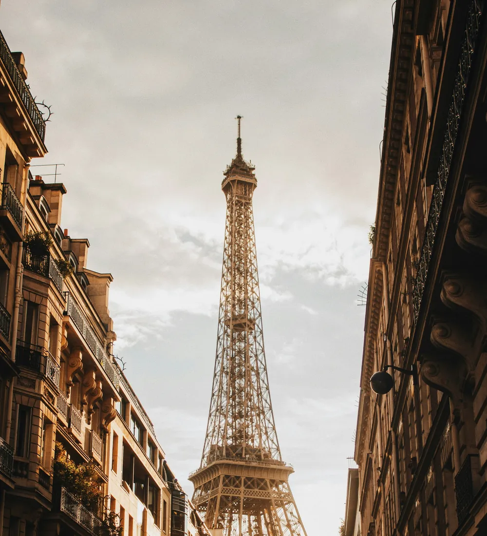 A Paris street with the Eiffel Tower rising between warm stone buildings